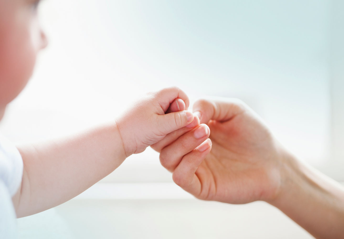 A baby holding an adult's finger